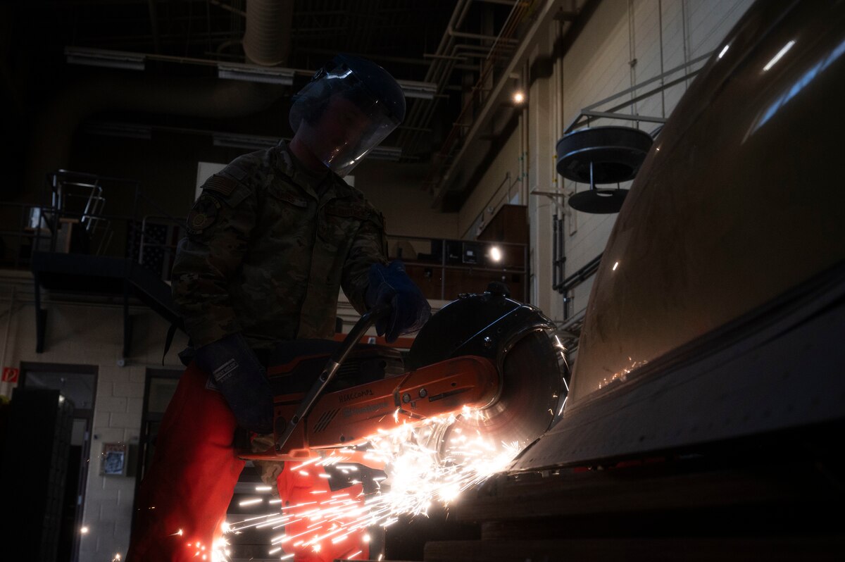 U.S. Air Force Staff Sgt. Nicholas Raines, 49th Equipment Maintenance Squadron crash recovery craftsman, saws through the side of an F-16 Viper during an exercise at Holloman Air Force Base, New Mexico, Nov. 20, 2023. The team’s proficiency is an extension of the sound communication between the supervisors and the Airmen, which demonstrates their prowess in leading and developing Airmen. (U.S. Air Force photo by Airman 1st Class Isaiah Pedrazzini)