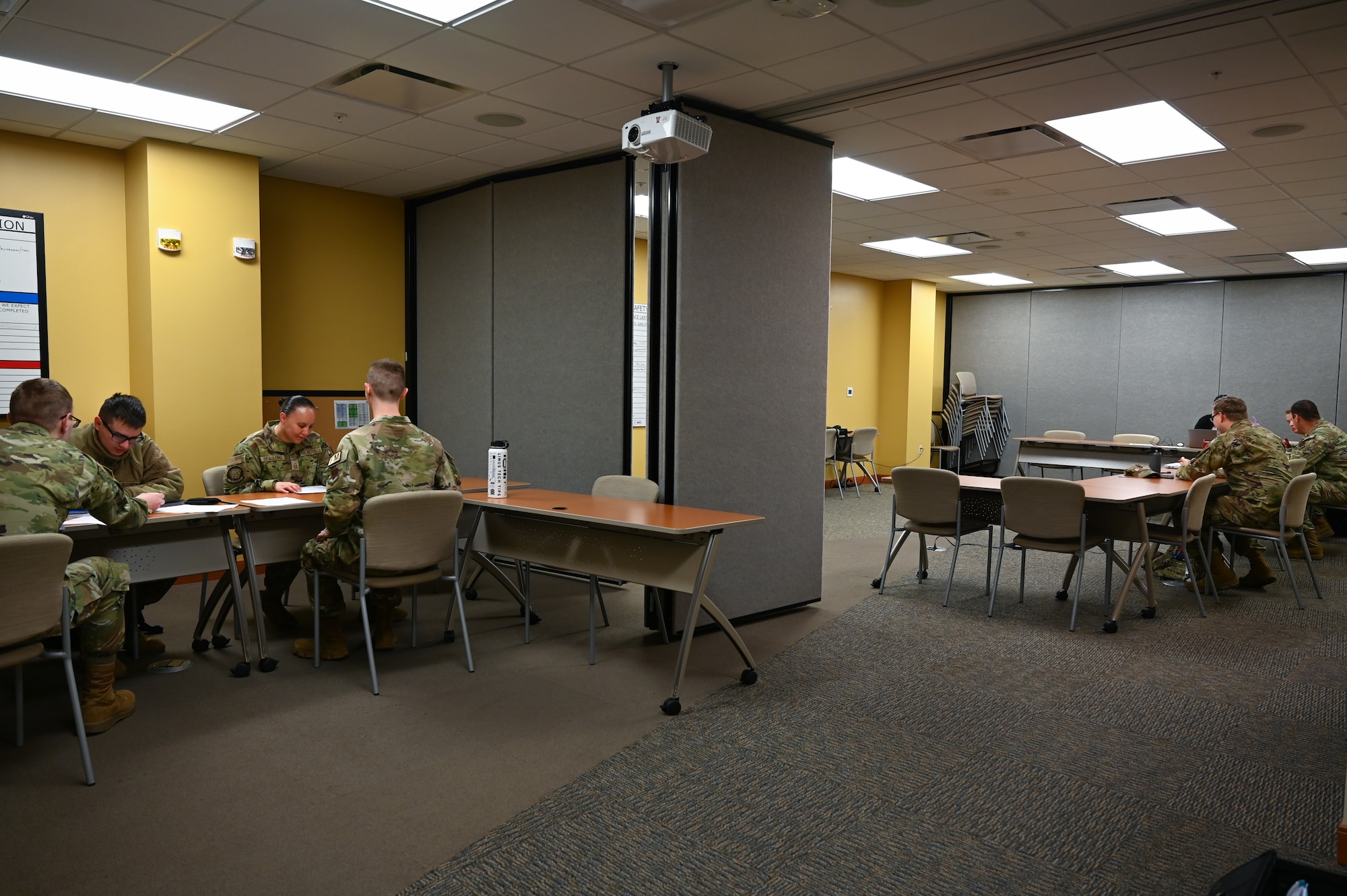 Overview of a room where there are two separate tables where Airmen are sitting down and talking