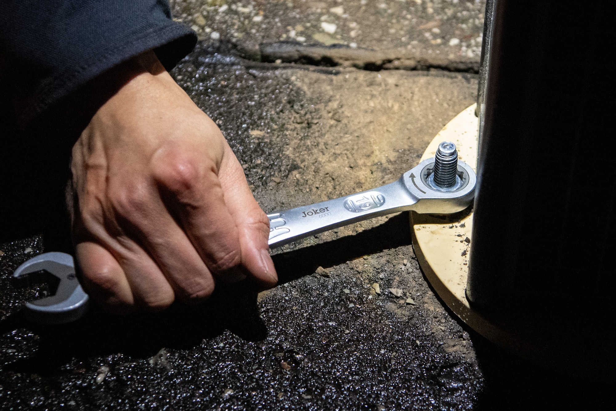 A hand uses a wrench to tighten a bolt to ground a light.
