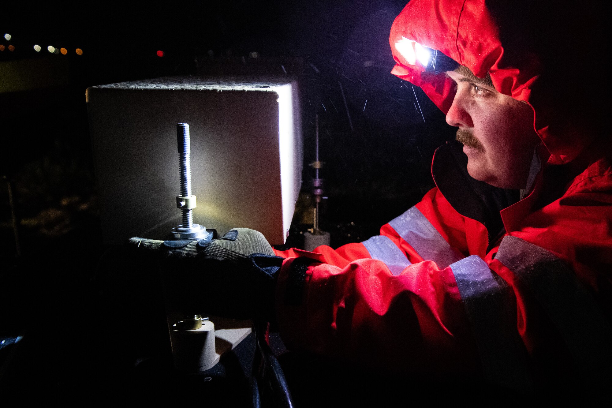 A man weaing a headlamp looks at his illumanted hands as they tighten a screw at night