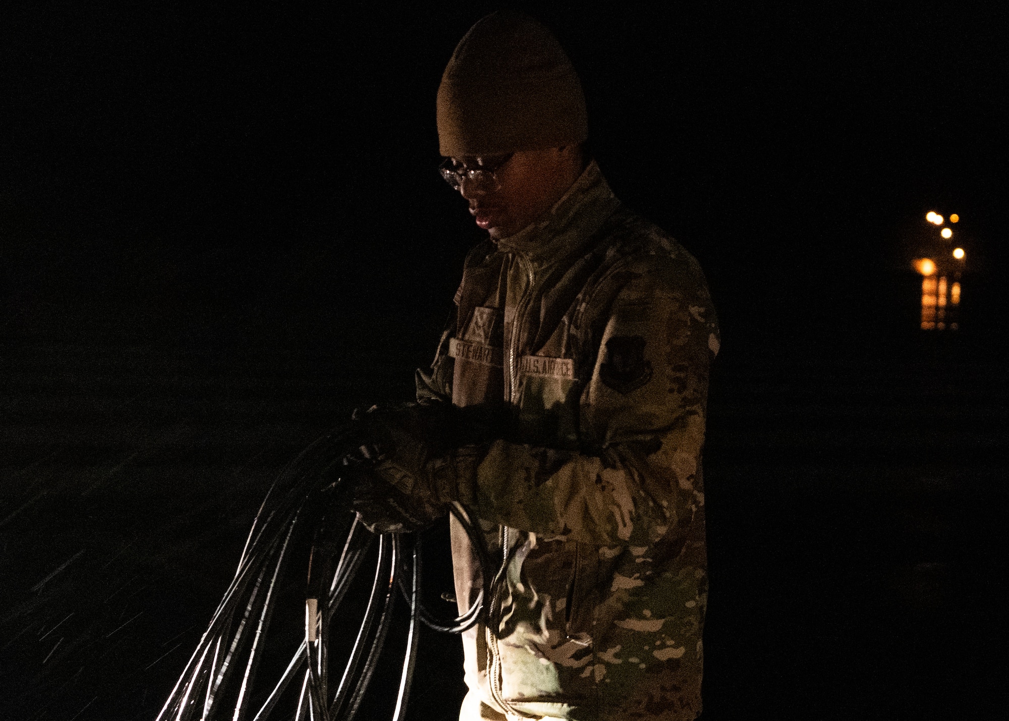 An Airmen holds a group of cables together at night.
