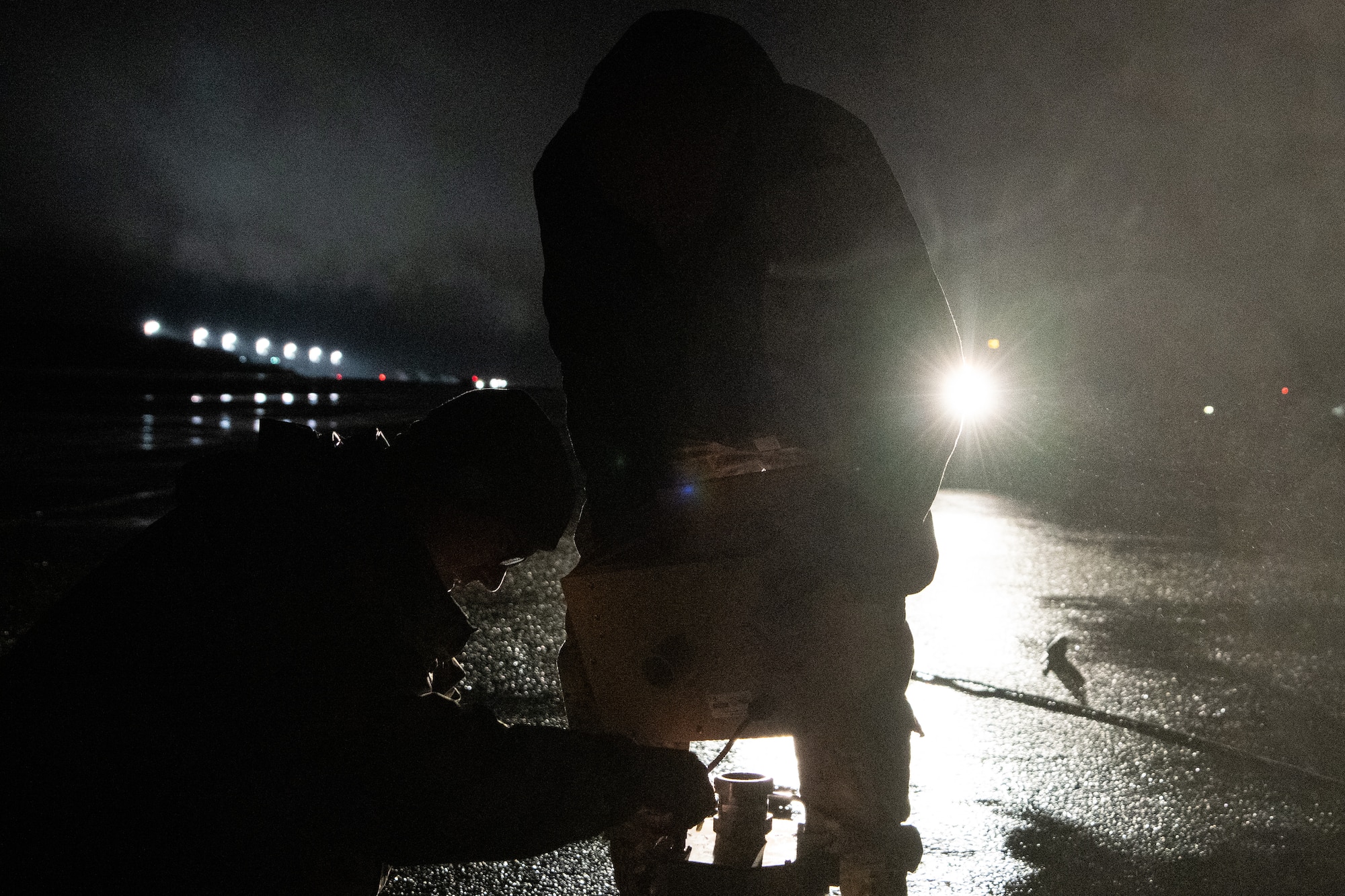 Two silhouetted Airmen install a runway light at night