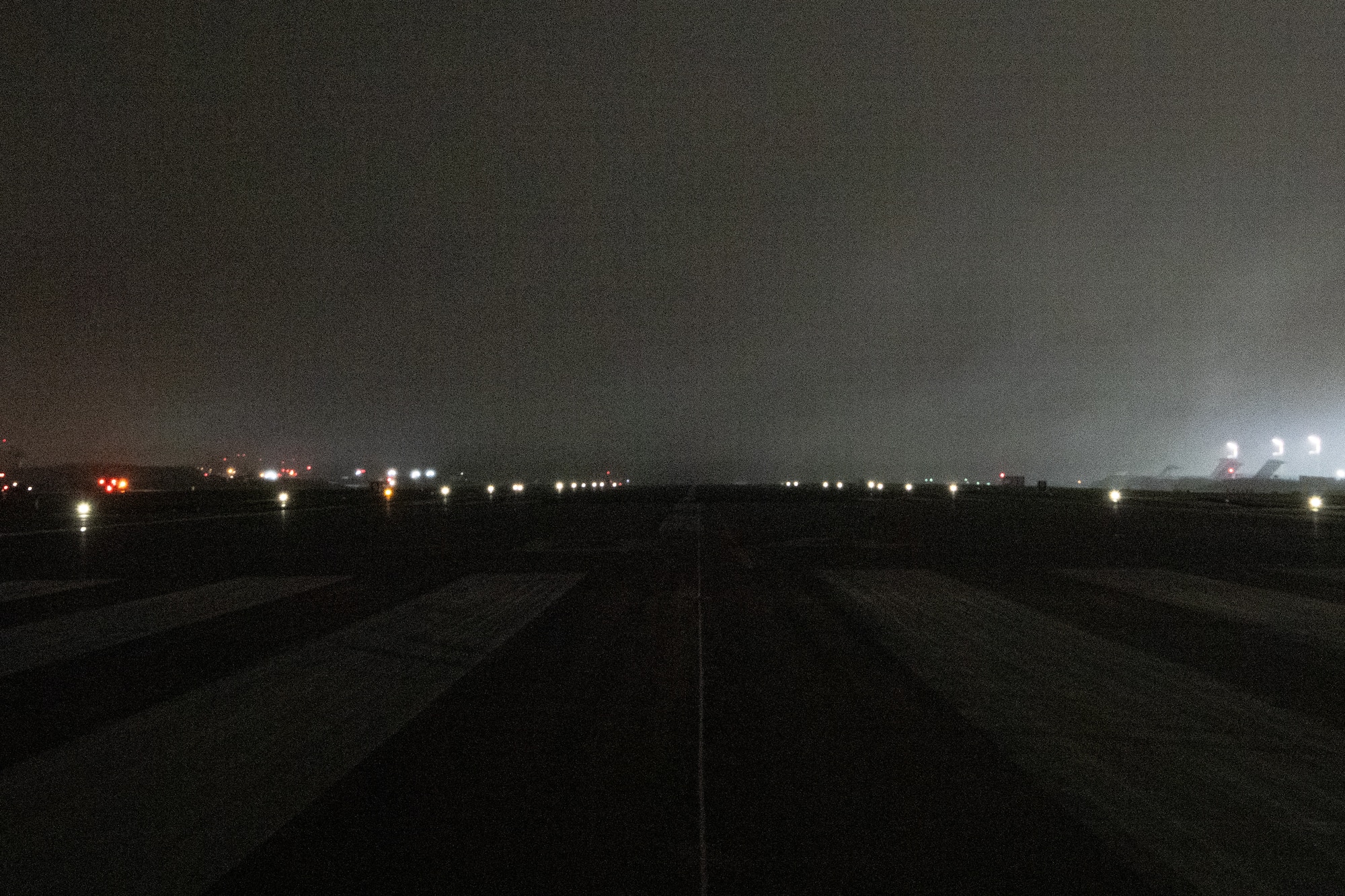 An airfield runway at night illuminated by lights along the edge.