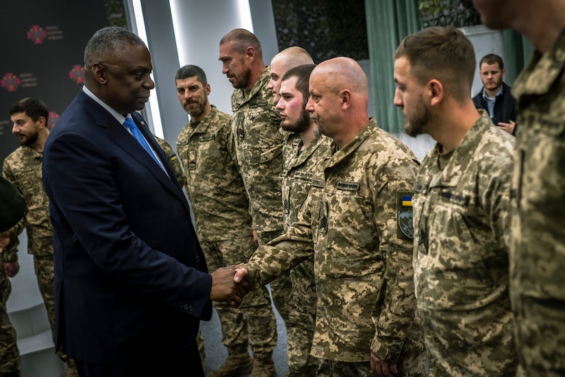 A person in a suit shakes hands with a man wearing a foreign military uniform.