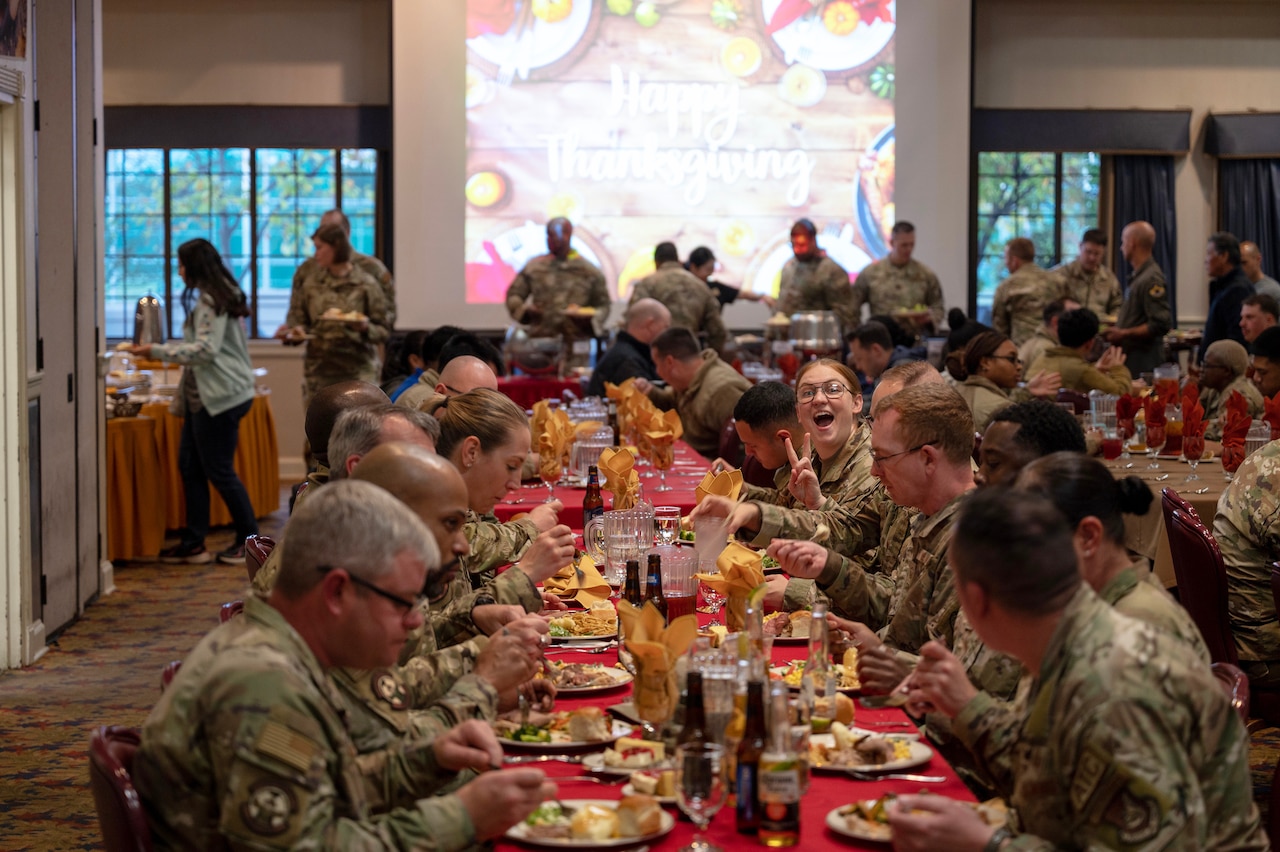 Service members are seated at tables to eat a Thanksgiving meal.