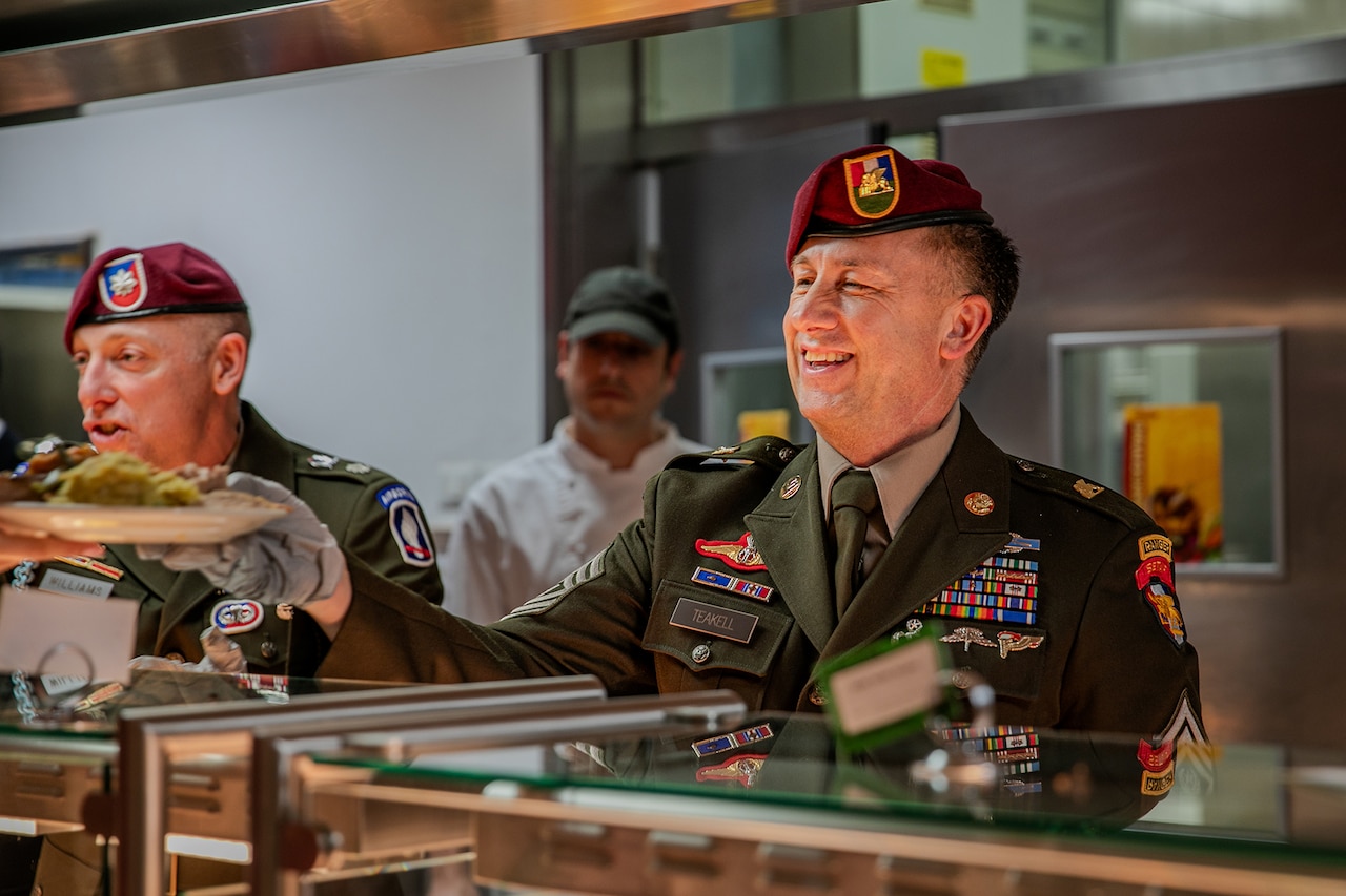 Service members serve Thanksgiving food from a buffet.
