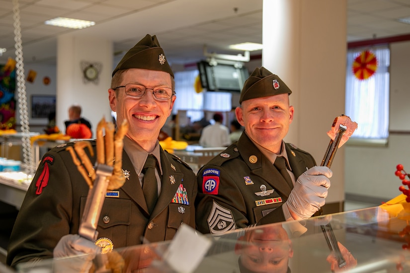 Service members serve Thanksgiving food from a buffet.