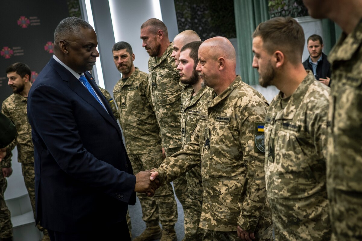 A person in a suit shakes hands with a man wearing a foreign military uniform.