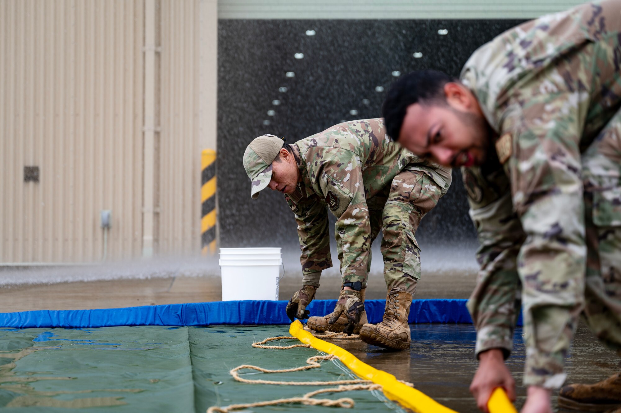 Two men conduct water mitigation procedures in a simulated storm during a Prime Base Engineer Emergency Force or “Prime BEEF” training at Kunsan Air Base