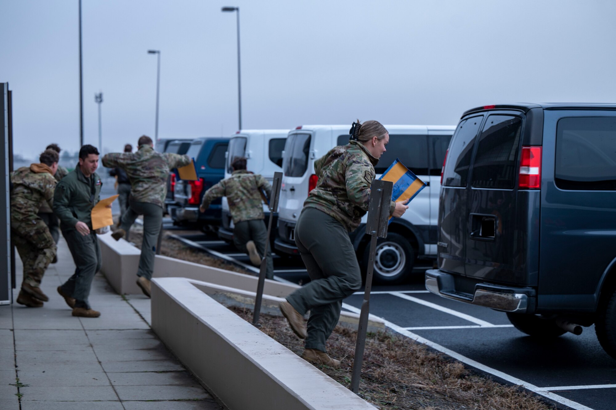 Airmen run to their cars in a parking lot.