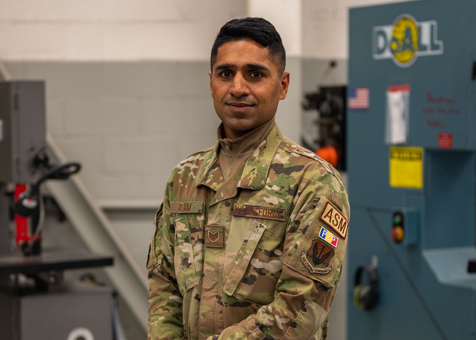 A man poses for a photo in a maintenance shop with a saw table behind him.