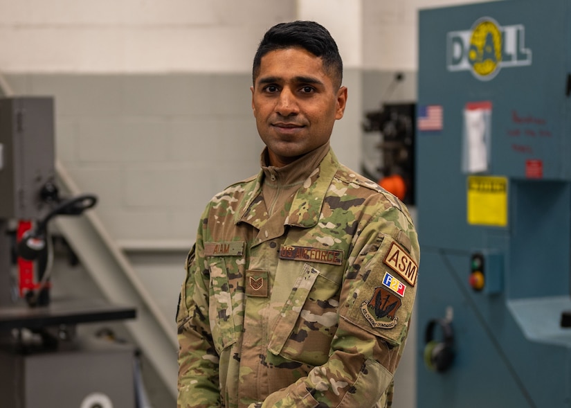A man poses for a photo in a maintenance shop with a saw table behind him.