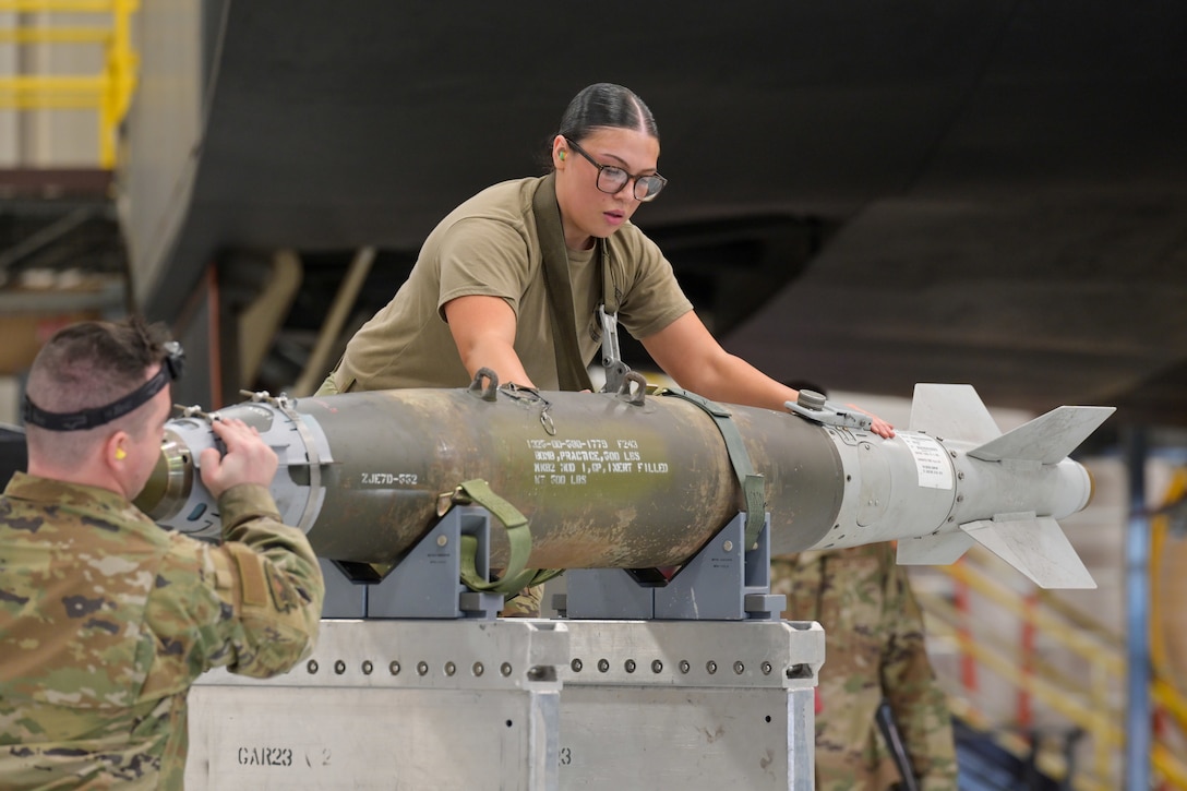 Two airmen hold a bomb on a rack.
