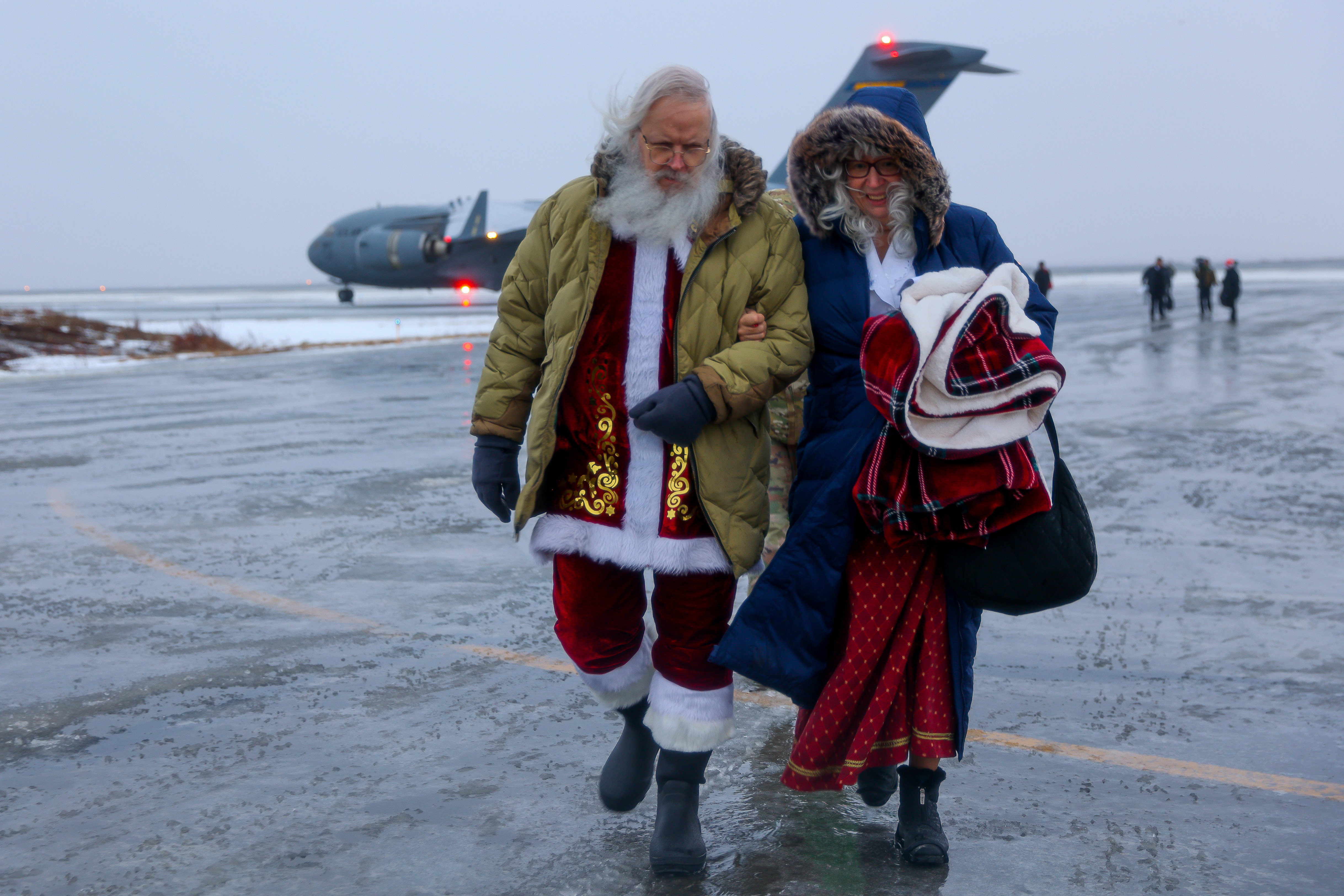 Santa and Mrs. Claus link arms while walking on a wet flight line.