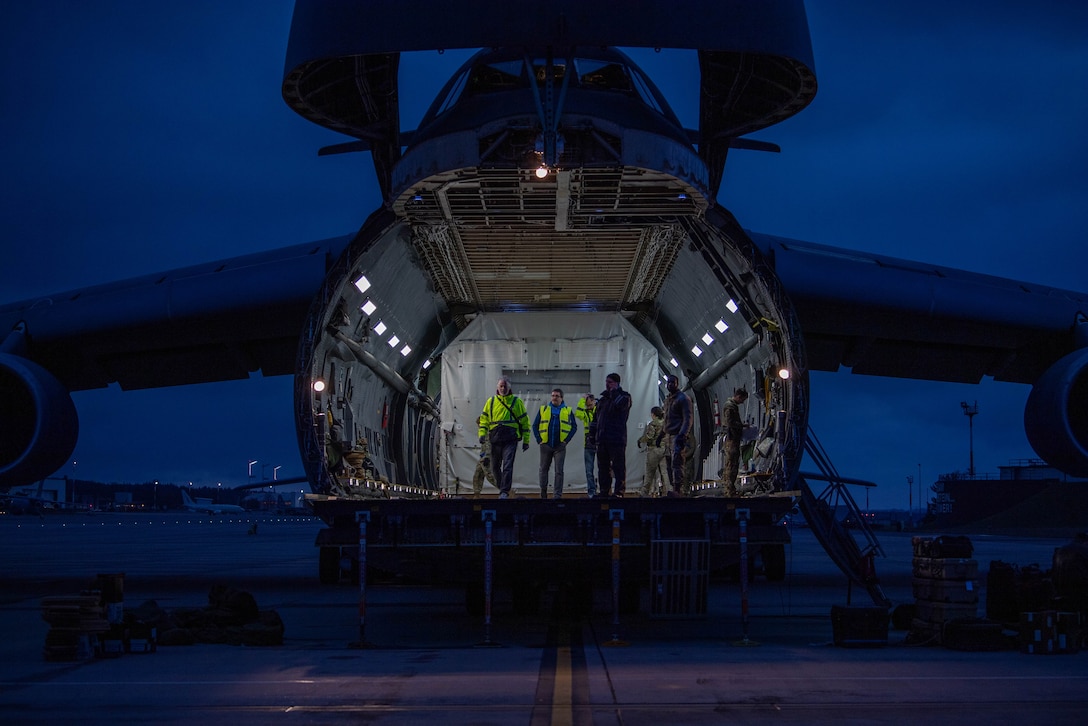 Airmen and civilians stand inside a military aircraft at night.