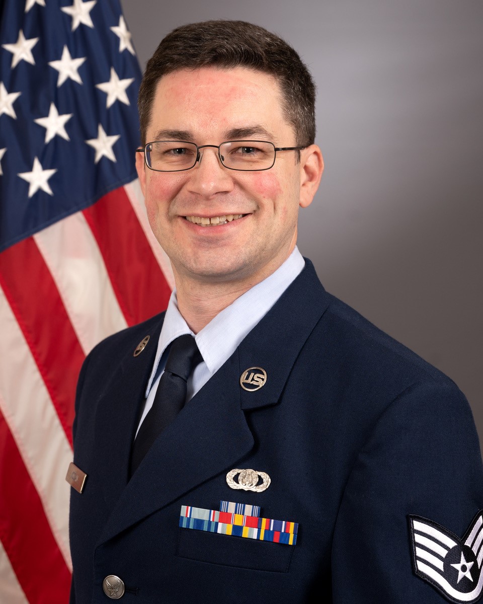 Official photo of SSgt Jarrett Kocan with American flag over right shoulder.
