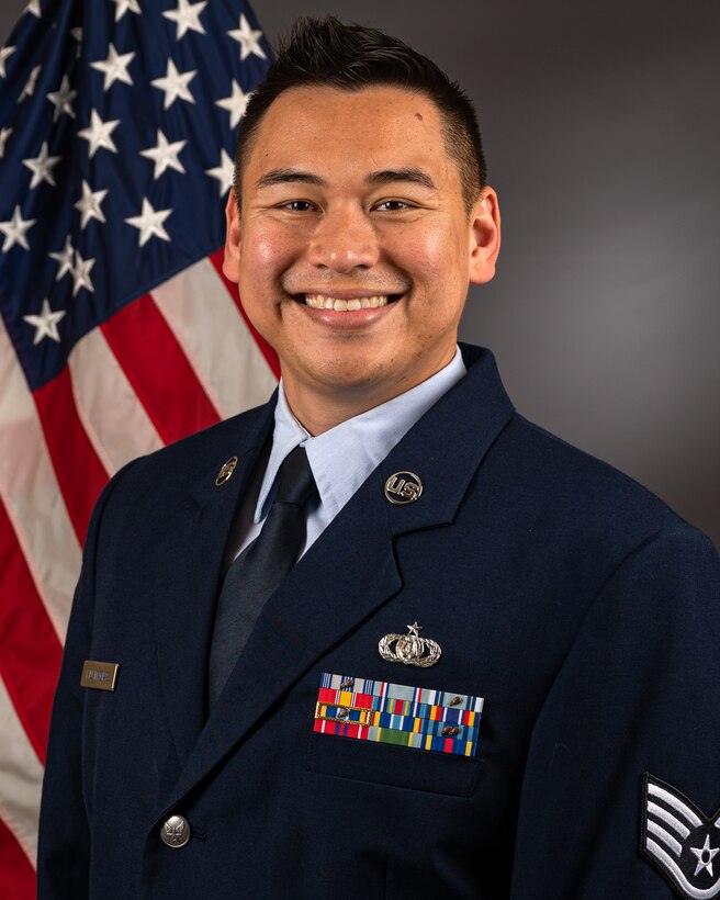 Official photo of SSgt Alex Liu Macias with American flag over right shoulder.