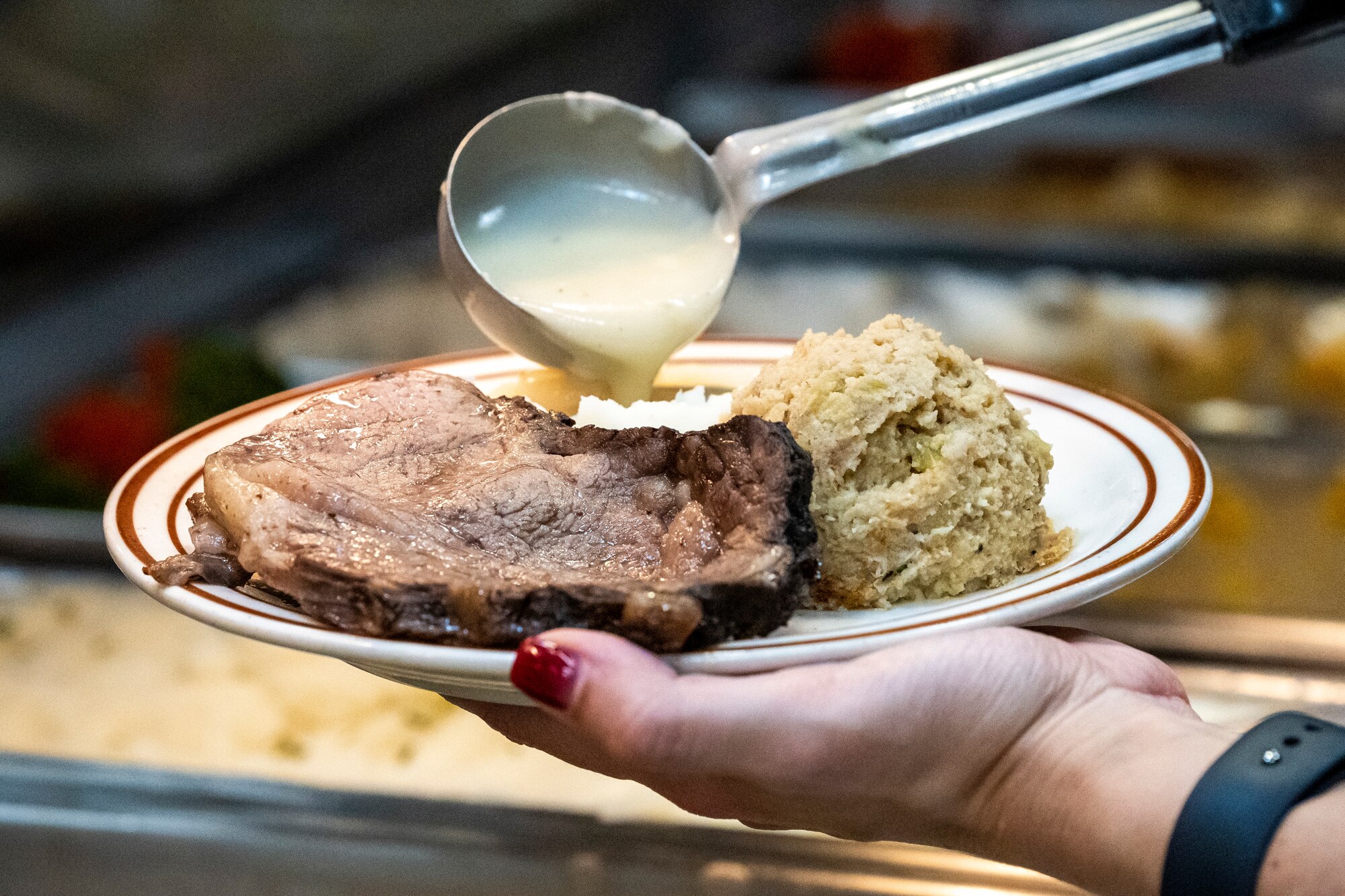 U.S. Air Force Lt. Col. Katherine Kuc, 81st Force Support Squadron commander, drizzles gravy onto an Airman's plate while serving a Thanksgiving meal to Airmen at Keesler Air Force Base, Mississippi, Nov. 23, 2023.