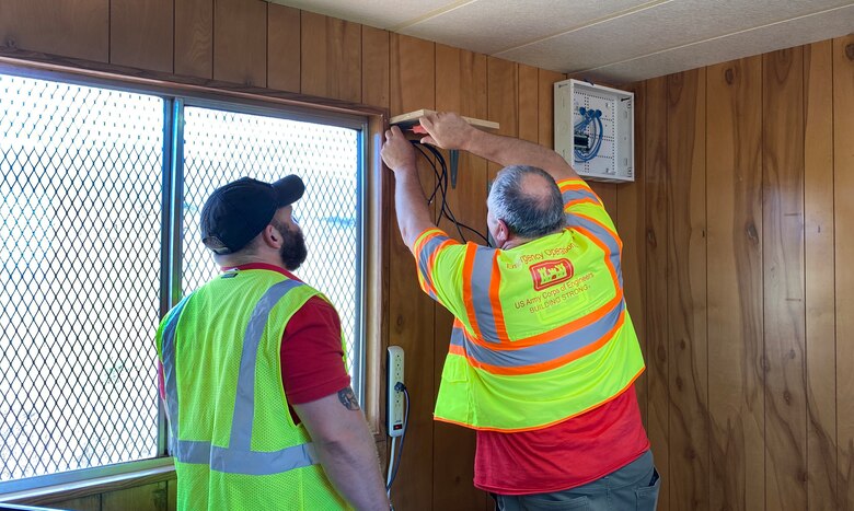 U.S. Army Corps of Engineers CIO/G6 Enterprise Emergency Response Team members Ryan Meersman and Dale Carton install a shelf in a construction trailer at the site where a temporary elementary school is being built.