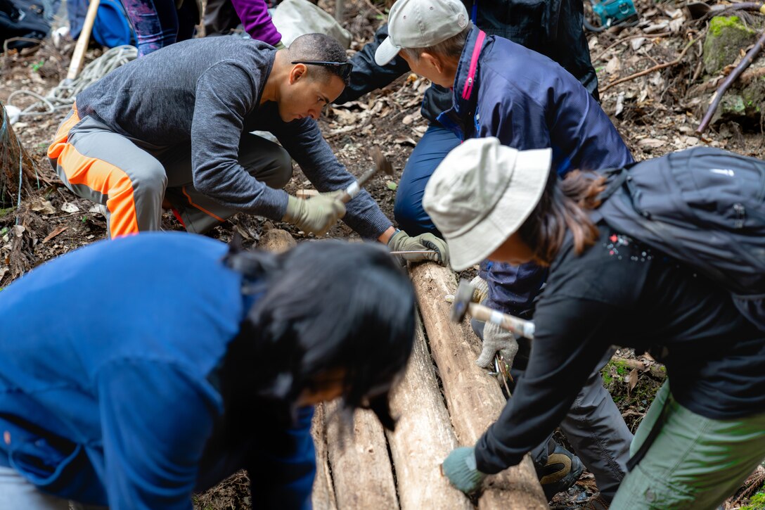 Fumio Shimohara, an Iwakuni, Japan, native, top right, and U.S. Marines from Marine Corps Air Station Iwakuni, hammer clamps into wooden logs during a community relations event at “Iwakuni Old Road,” Miwa Town, Iwakuni, Japan, Nov. 16, 2023. Service members from Marine Corps Air Station Iwakuni have been helping locals maintain the road since 2005 to reinforce the relationship between MCAS Iwakuni and the local Japanese community (U.S. Marine Corps photo by Cpl. Raymond Tong).