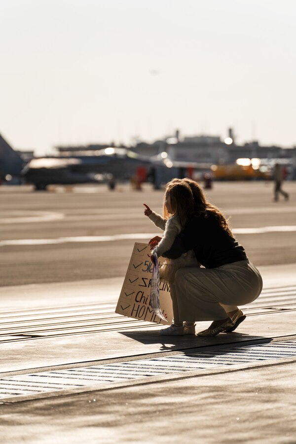 A military spouse and child wait for Sailors of Strike Fighter Squadron (VFA) 102, Carrier Air Wing (CVW) 5 to return from deployment ,Marine Corps Air Station Iwakuni, Japan, Nov. 20 2023. CVW-5’s return marked the completion of their most recent deployment aboard the USS Ronald Reagan (CVN -76), where they projected airpower in support of a free and open Indo-Pacific. (U.S. Marine Corps photo by Lance Cpl. Brian Long)