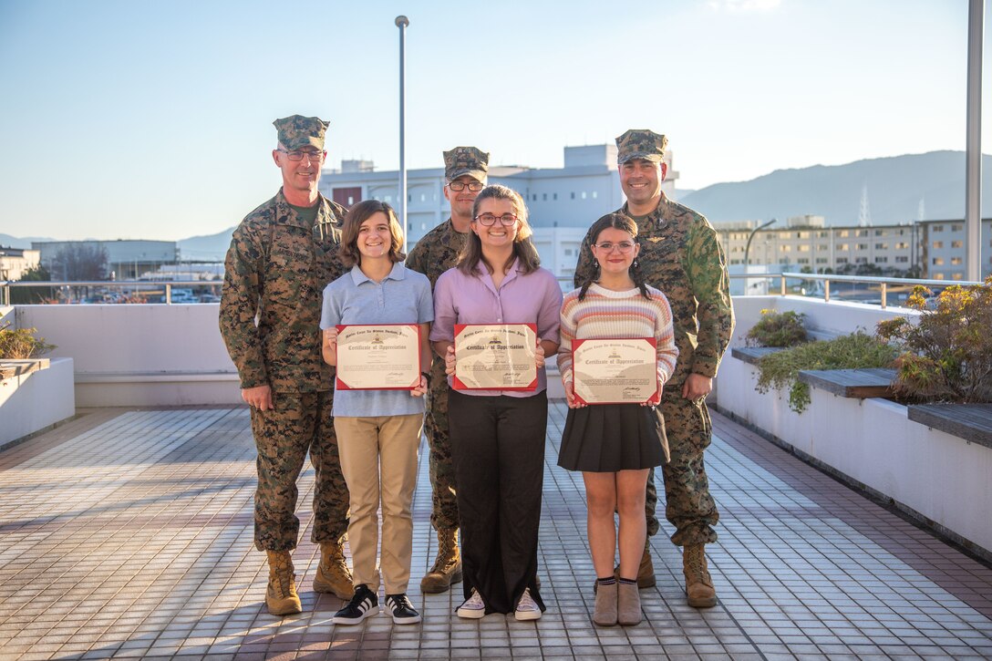 U.S. Marine Corps Master Sgt. Dylan Theberge, center, an aviation supply specialist with Marine Aviation Logistics Squadron (MALS) 12, Marine Aircraft Group (MAG) 12, and his daughters pose for a photo with Sgt. Maj. Jody Armentrout, left, the sergeant major of Marine Corps Air Station Iwakuni, and Col. Richard Rusnok, right, the commanding officer of Marine Corps Air Station Iwakuni, during the October Impact Iwakuni award presentation at MCAS Iwakuni, Japan, Nov. 15, 2023. Master Sgt. Theberge and his daughters are soccer coaches for 3- and 4-year-olds in the youth sports program and were recognized by the air station for their efforts in making a substantial impact on the community. (U.S. Marine Corps photo by Cpl. Calah Thompson)