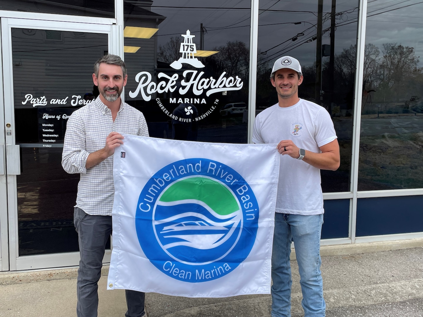 Two men stand holding a flag that says clean marina.