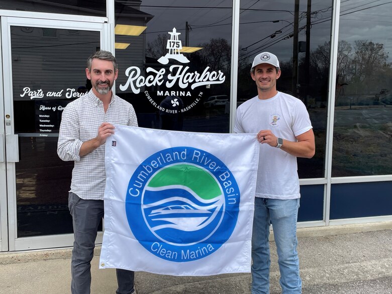 Two men stand holding a flag that says clean marina.