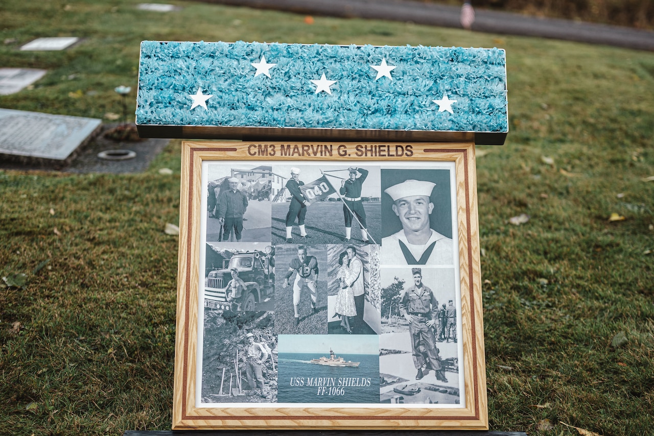 A commemoration plaque and ribbon are displayed in a cemetery.