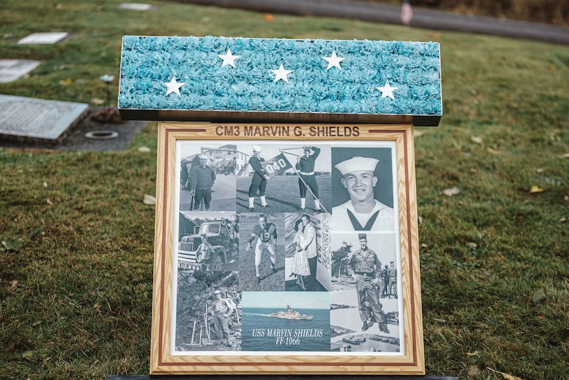 A commemoration plaque and ribbon are displayed in a cemetery.