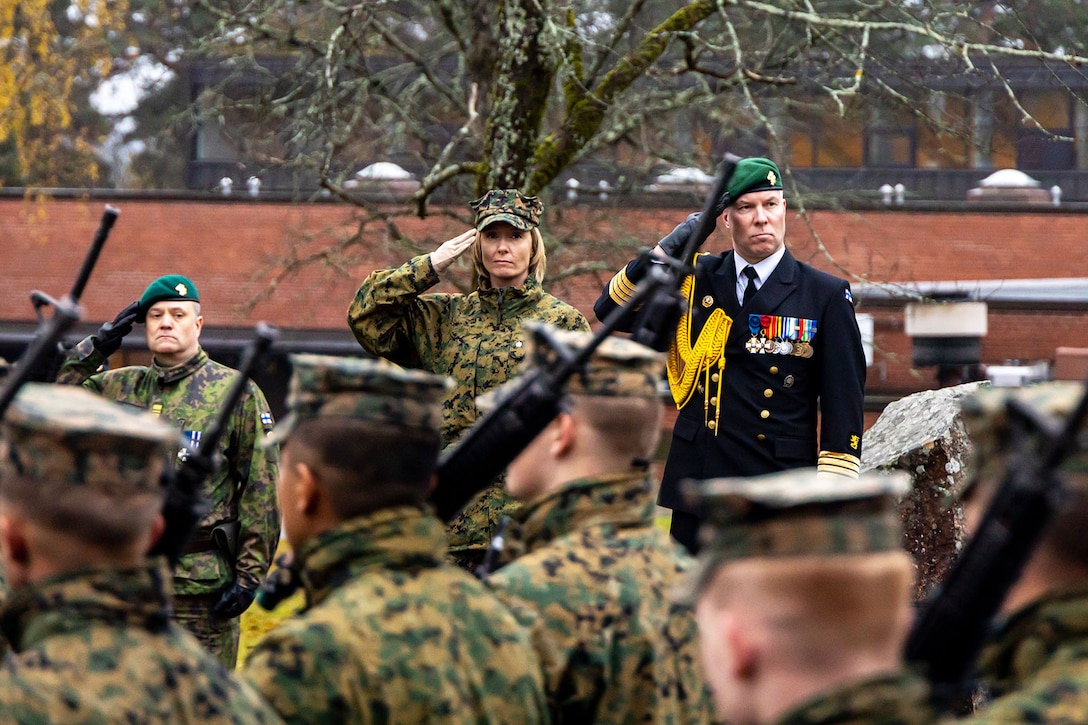 Military  officers salute Marines and Finnish soldiers as they march by.