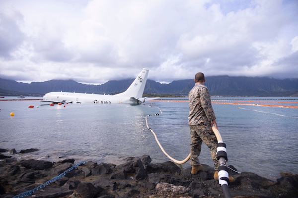 A U.S. Marine holds a fuel hose being secured during defueling operations on a downed U.S. Navy P-8A Poseidon in waters just off the runway at Marine Corps Air Station Kaneohe Bay, Marine Corps Base Hawaii, Nov. 26, 2023.