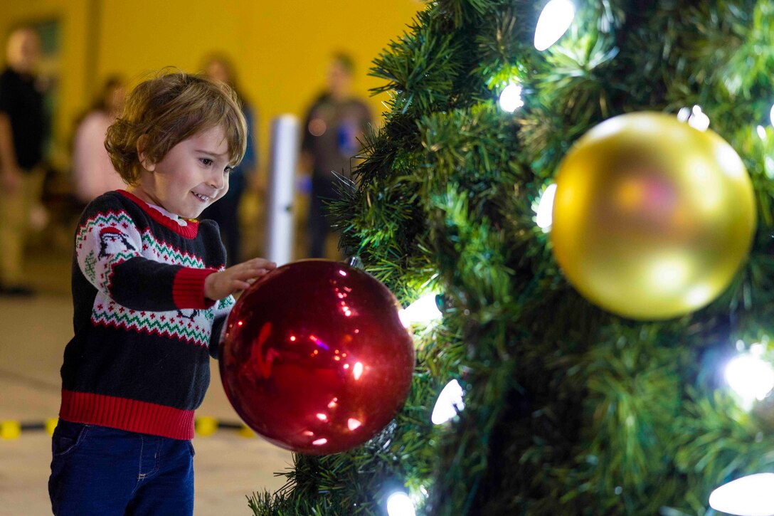 A child touches an ornament on a tree.
