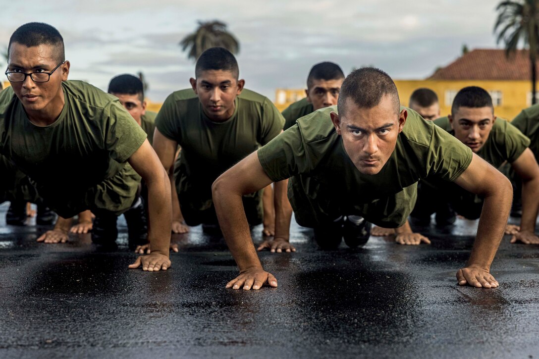 Dozens of Marines perform pushups on wet pavement.