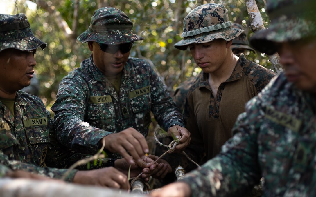 Philippine Marines with Marine Battalion Landing Teams 8 and 10 teach U.S. Marine Corps Lance Cpl. Logan Evans, an infantry rifleman with 3d Littoral Combat Team, Marine Littoral Regiment, 3d Marine Division, how to use winding vines as twine during a jungle shelter class during KAMANDAG 7 at Paredes Air Station, Philippines, Nov. 10, 2023. KAMANDAG is an annual Philippine Marine Corps and U.S. Marine Corps-led exercise aimed at improving multinational readiness, relationships, and mutual capabilities in the advancement of a Free and Open Indo-Pacific. This year marks the seventh iteration of this exercise and includes participants from Japan, the Republic of Korea, and observers from the United Kingdom. Evans is a native of Huntley, Ill. (U.S. Marine Corps photo by Sgt. Jacqueline C. Parsons)