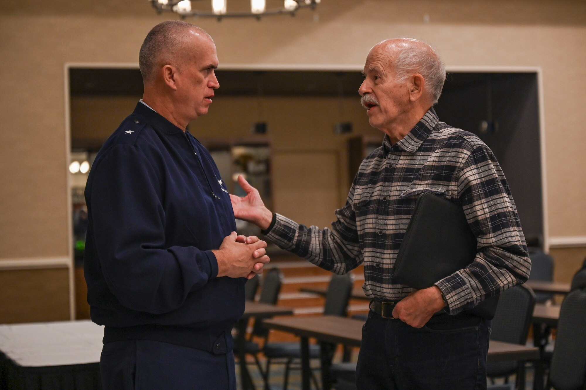 Two men face each other as they speak in a conference room.