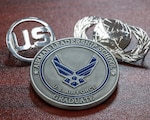 The Airman Leadership School graduate coin being presented alongside the U.S. symbol and the Public Affairs occupational badge at Laughlin Air Force Base, Texas, Nov 17, 2023. Coins are given to ALS graduates upon completion of the course and shows proof of the graduation. (U.S. Air Force photo by Staff Sergeant Nicholas Larsen)