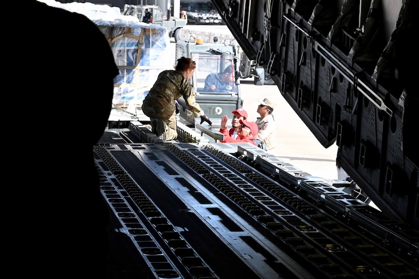 A female airman leans forward to talk to men loading cargo into an aircraft.