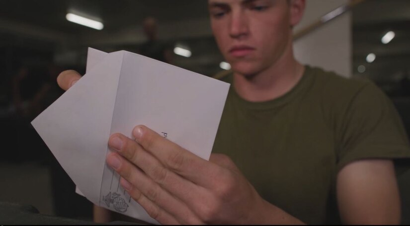 A Marine Corps recruit puts a letter in an envelope.