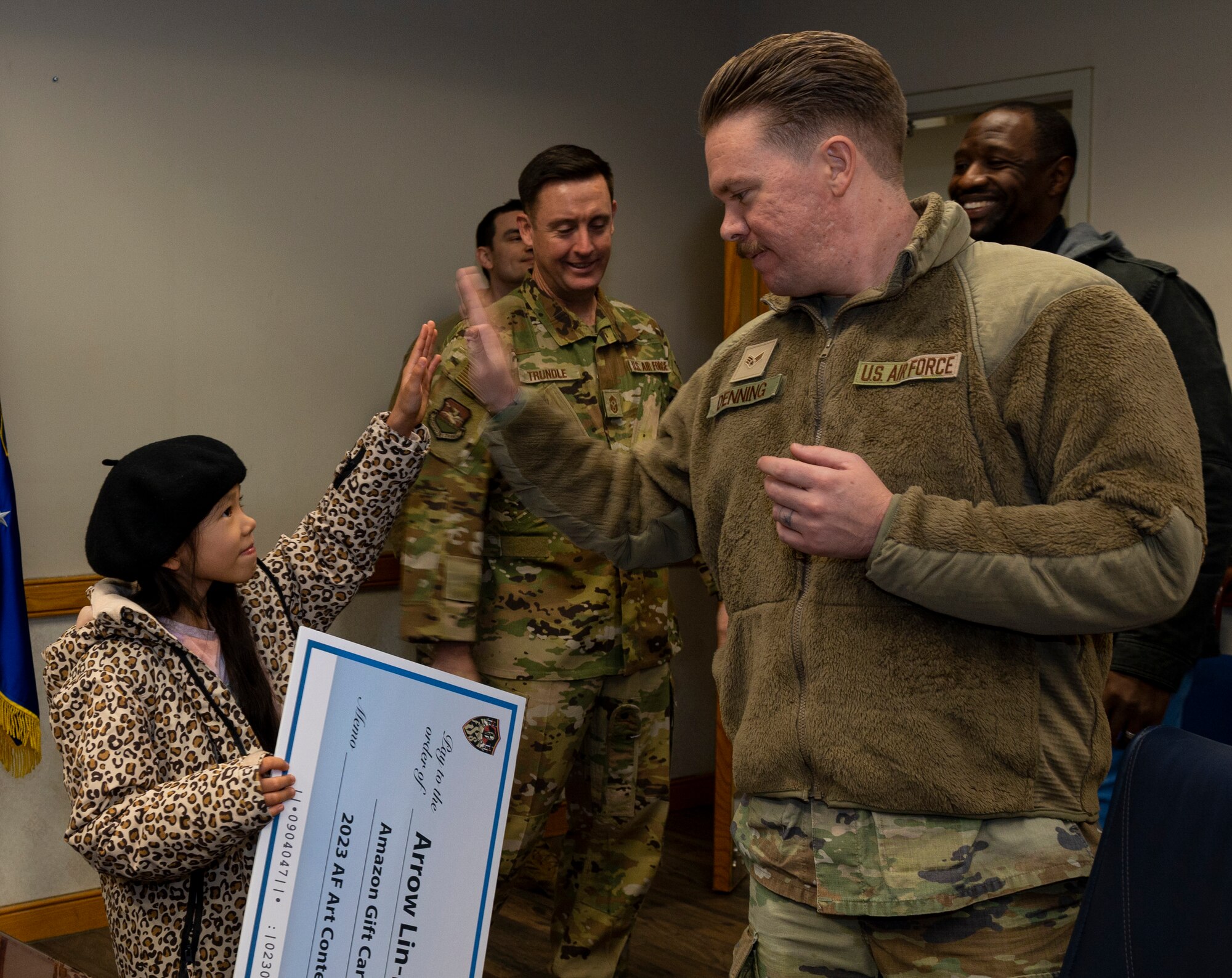 Arrow Lin-Denning, daughter of U.S. Air Force Senior Airman Michael Denning, 607th Combat Weather Squadron weather forecaster, high fives her dad after receiving a gift card for placing in the 2023 Air Force Art Contest at Osan Air Base, Republic of Korea, Nov. 27, 2023. Lin-Denning won second in the Youth 3D Art six to eight year old category. Her piece is being displayed at the San Antonio airport. (U.S. Air Force photo by Senior Airman Kaitlin Castillo)