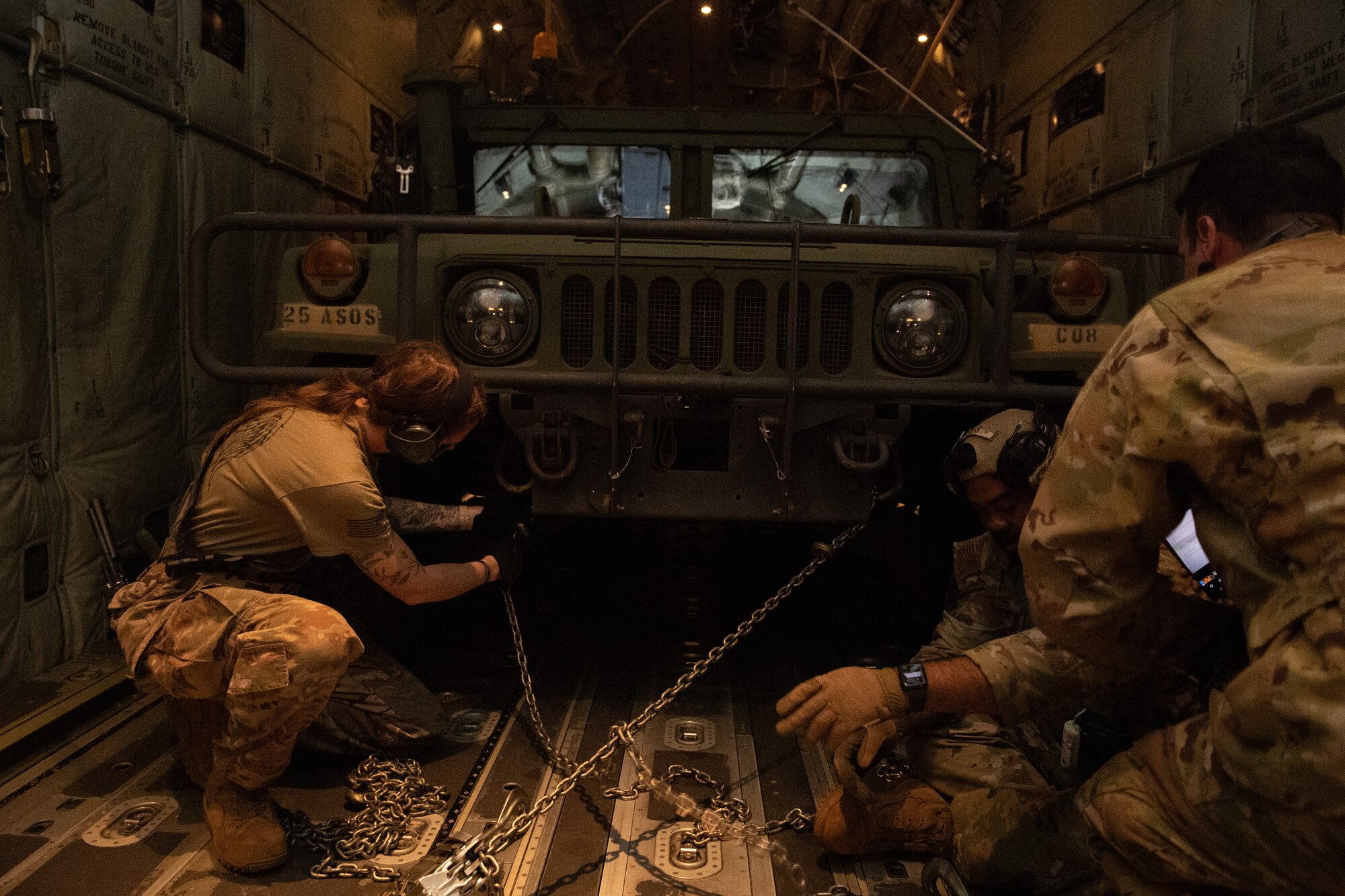 Airmen secure chains holding a humvee to an aircraft.