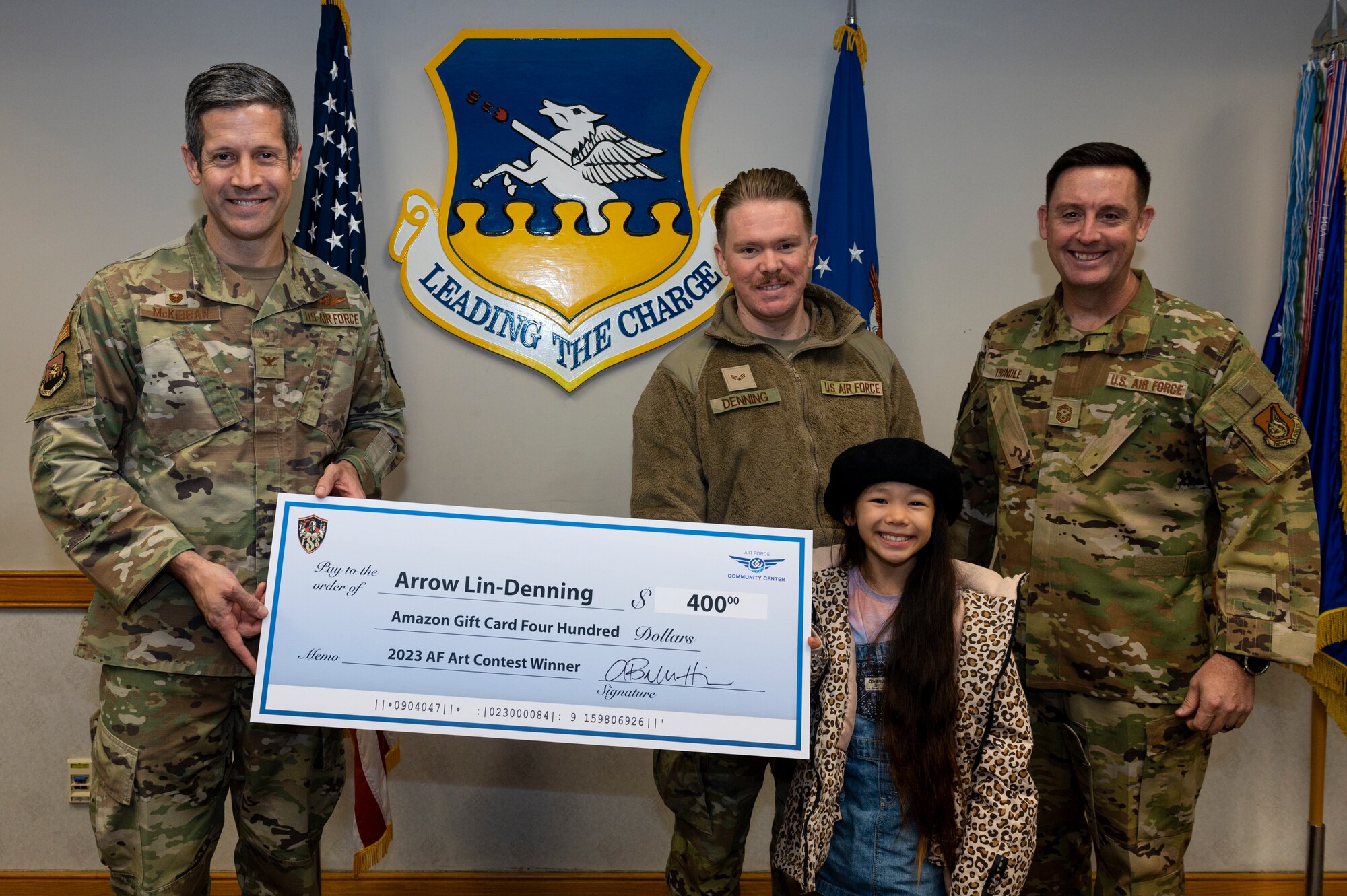 U.S. Air Force Col. William McKibban, 51st Fighter Wing commander, and Chief Master Sgt. Joshua Trundle, 51st FW command chief, present Arrow Lin-Denning, daughter of Senior Airman Michael Denning, 607th Combat Weather Squadron weather forecaster, with a gift card at Osan Air Base, Republic of Korea, Nov. 27, 2023. Lin-Denning won second place in the 2023 Air Force Art Contest in the Youth 3D Art six to eight year old category. (U.S. Air Force photo by Senior Airman Kaitlin Castillo)