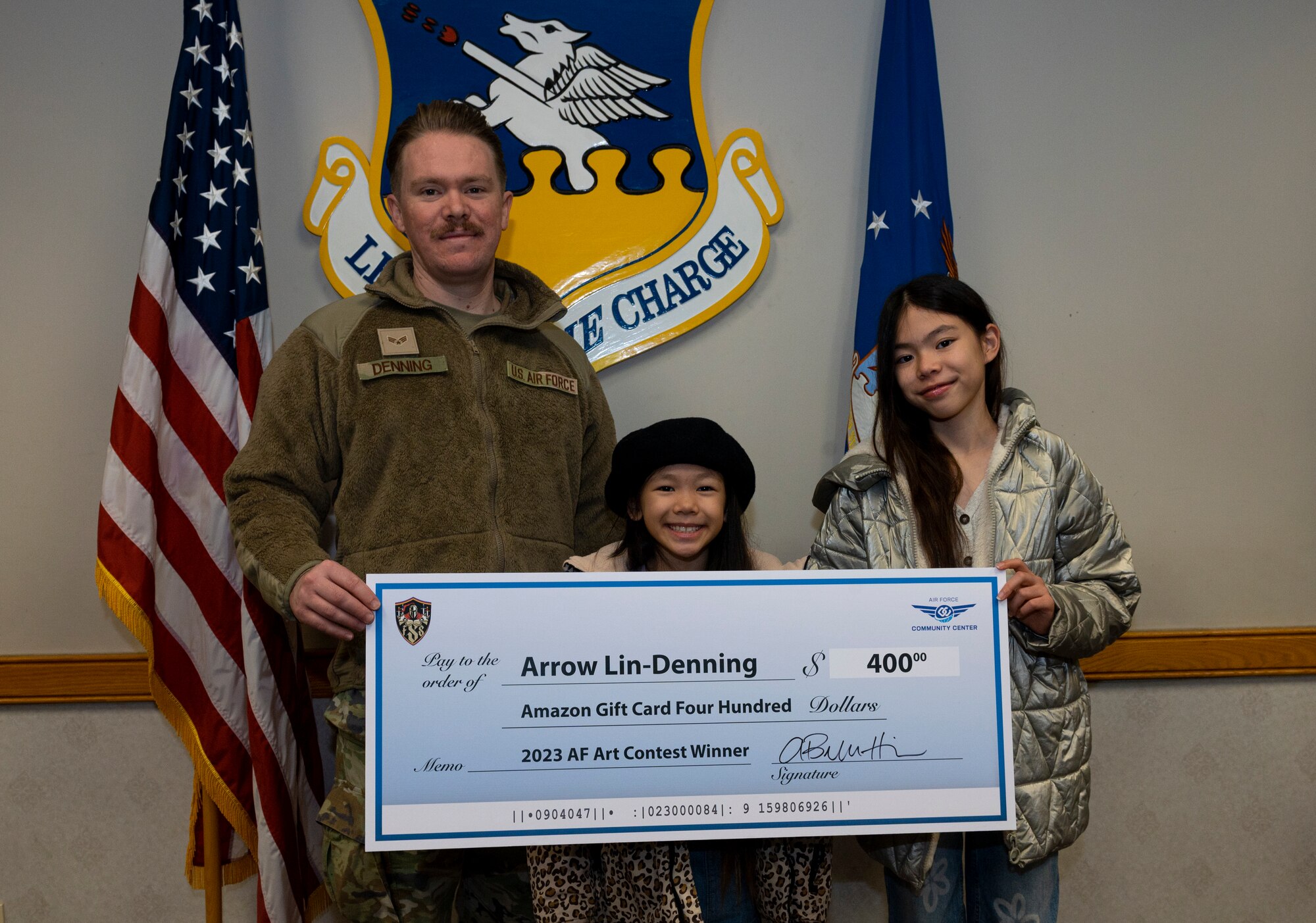 U.S. Air Force Col. William McKibban, 51st Fighter Wing commander, and Chief Master Sgt. Joshua Trundle, 51st FW command chief, present Arrow Lin-Denning, daughter of Senior Airman Michael Denning, 607th Combat Weather Squadron weather forecaster, with a gift card at Osan Air Base, Republic of Korea, Nov. 27, 2023. Lin-Denning won second place in the 2023 Air Force Art Contest in the Youth 3D Art six to eight year old category. (U.S. Air Force photo by Senior Airman Kaitlin Castillo)