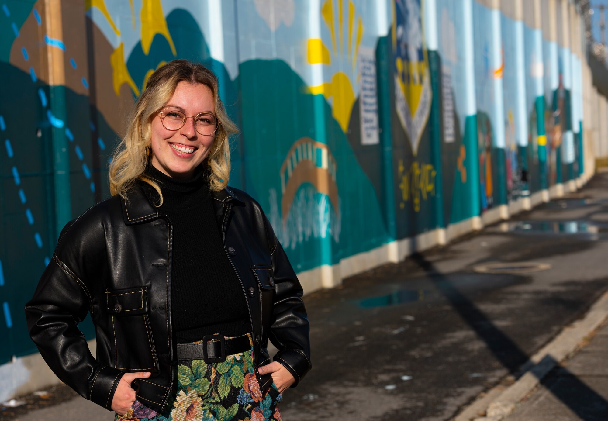 Tenley Brady, spouse of 1st Lt. Tre Brady, 303rd Intelligence Squadron flight commander and lead painter, stands in front of the new mural at Osan Air Base, Republic of Korea, Nov. 28, 2023. Brady and her spouse 1st Lt. Tre Brady, 303rd Intelligence Squadron flight commander, began designing the 4,410 square foot mural in May. The mural was completed in an effort to showcase appreciation for Korean culture. (U.S. Air Force photo by Senior Airman Kaitlin Castillo)