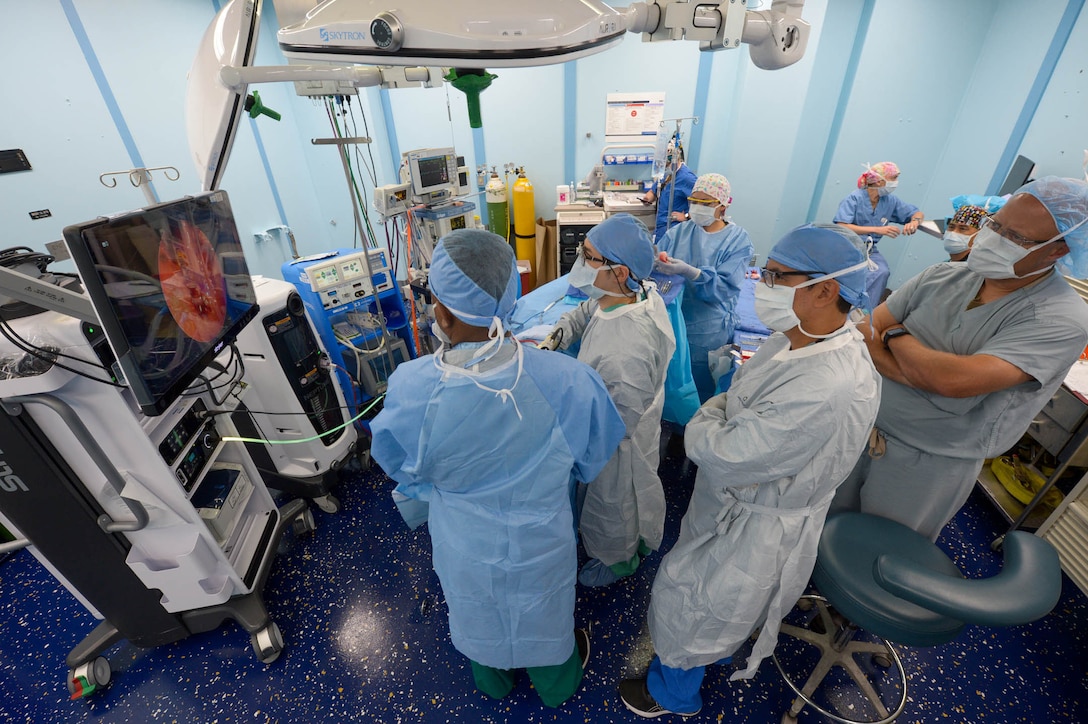 A group of sailors in medical uniforms look at a screen in an operating room.