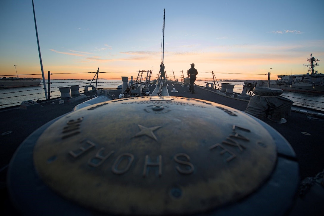 A sailor lowers a flag at sunset.