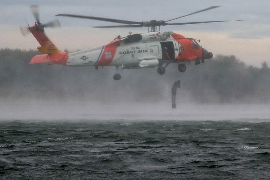 A service member jumps from a helicopter into open waters on a cloudy day.