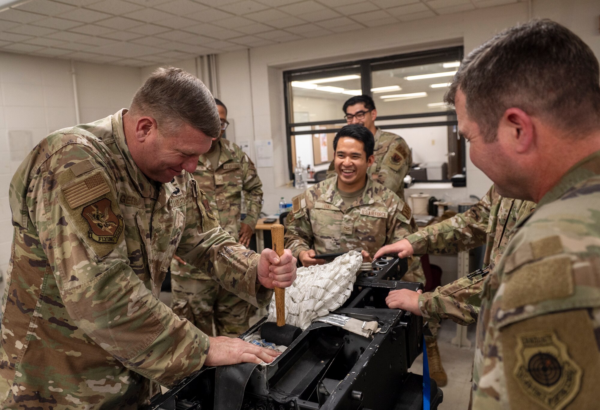 U.S. Air Force Chief Master Sgt. Justin Geers, 23rd Wing command chief, left, hammers down a parachute with a mallet at Moody Air Force Base, Georgia, Nov. 20, 2023. Rubber mallets are used to ensure the snug fit of the parachute in the back of the ejection seat. (U.S. Air Force photo by Airman 1st Class Leonid Soubbotine)