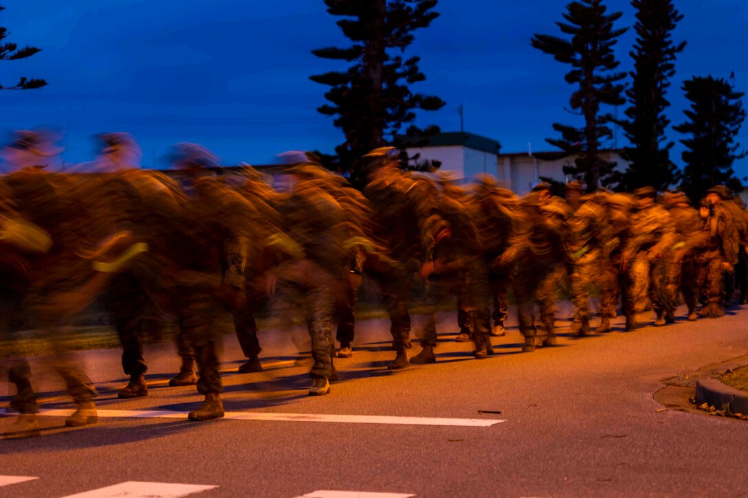 A blurred view of Marines and sailors walking in formation under a dark sky.
