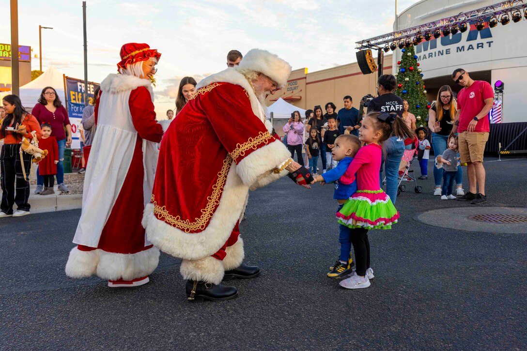 Two children meet Mr. and Mrs. Santa Claus while others stand around.